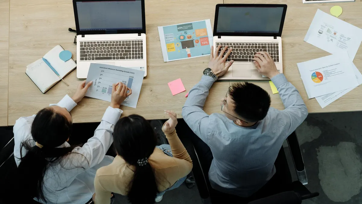 Three colleagues working on laptops and documents collaborating on the commercial operations of a business