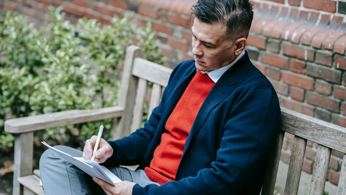 Profesional de ventas escribiendo notas en un cuaderno con documentación sobre una mesa al aire libre