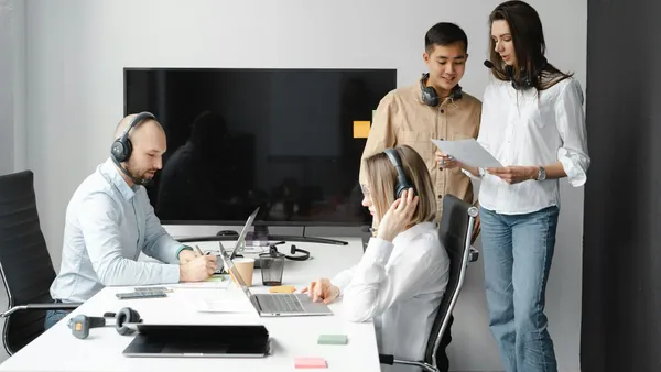 Equipo profesional colaborando en una oficina moderna con portátiles y auriculares
