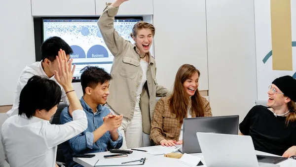 Small sales team gathered around a laptop in a modern office reviewing sales data