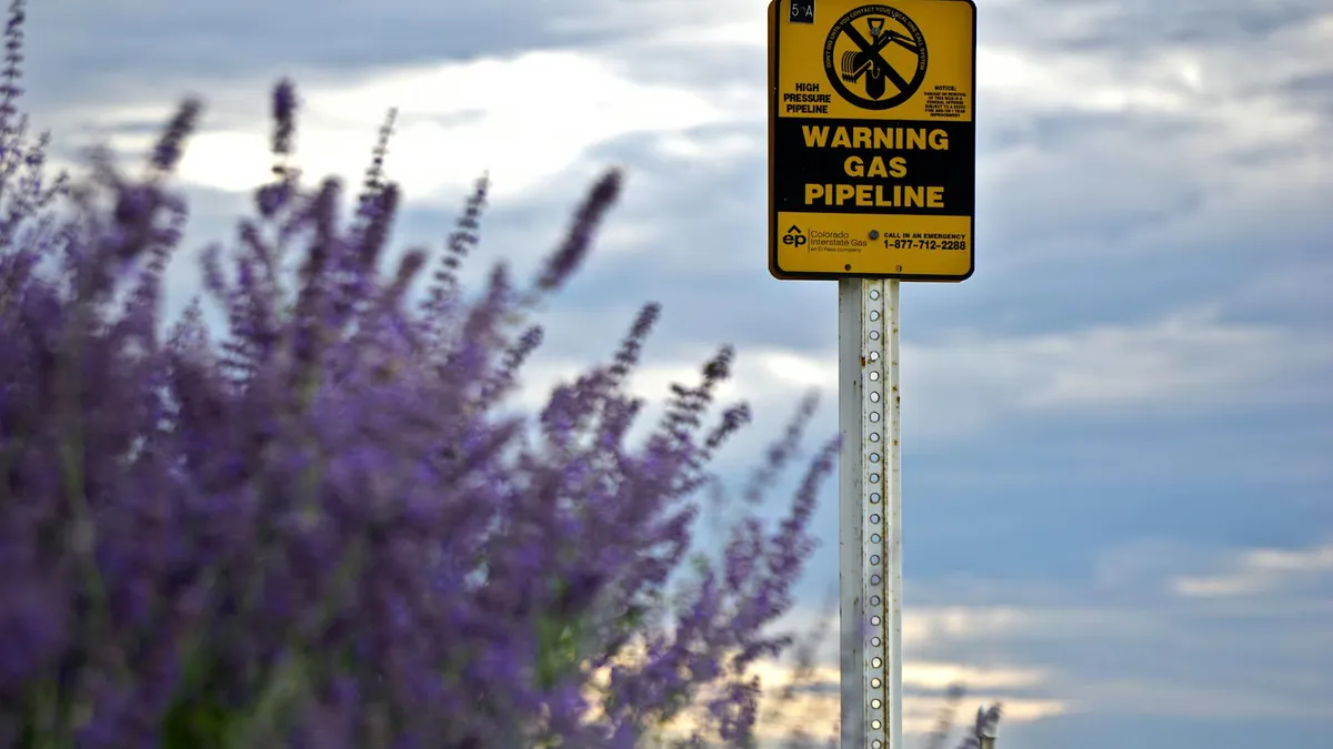 Panneau d'avertissement sur un gazoduc entouré de champs de lavande en fleur, métaphore des signaux d'alerte dans un pipeline commercial