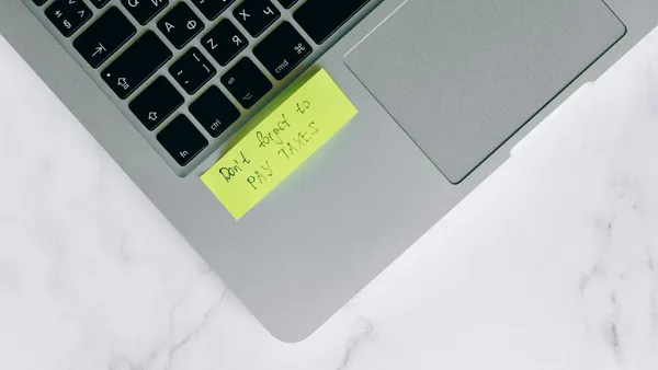 Laptop with sticky note about digital tax obligations in a modern office